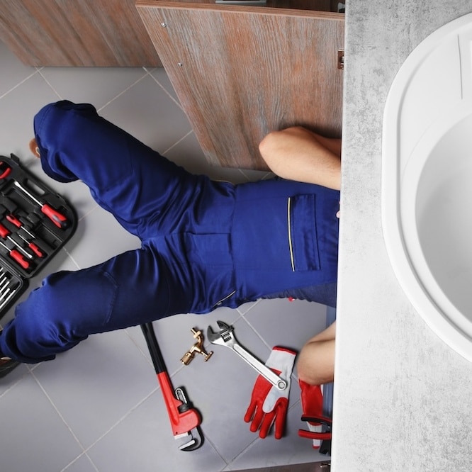 A plumber is working on the pipes underneath a sink.